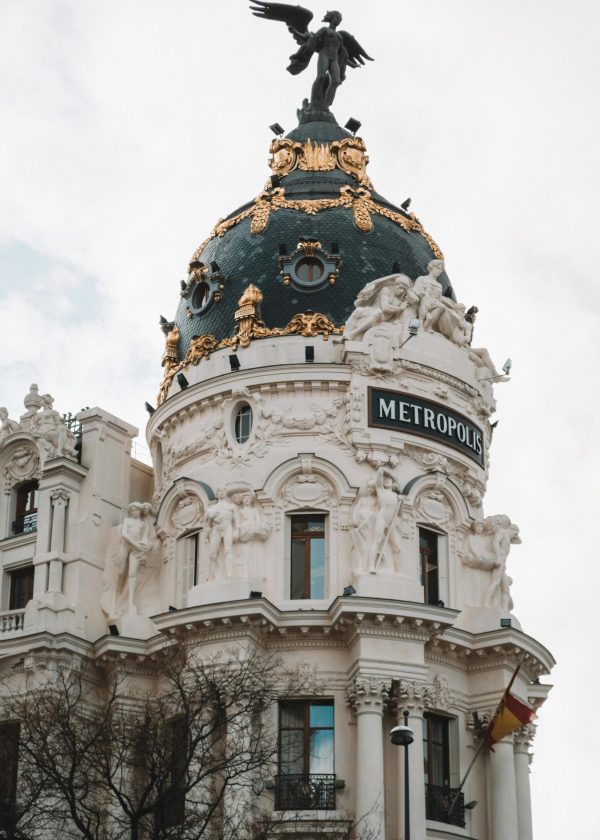 Iconic Metropolis Building dome in Madrid captured in daylight, showcasing intricate architectural details and sculptures.